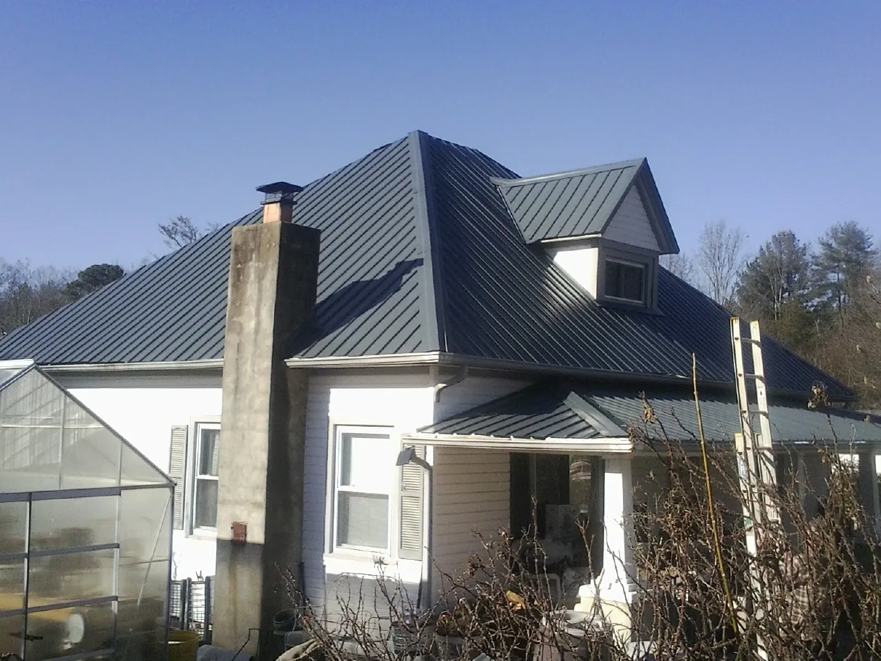 Dark blue standing seam metal roof on a white farmhouse with dormer — Slate & Tile Roof Repair by Roofing Brothers in Gilman