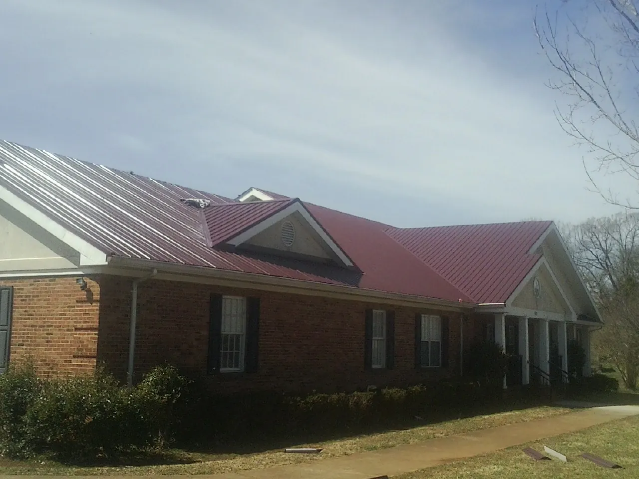 Red metal roof with gabled entries on a long brick building, from a Hail Damage Roof Repair job in Gilman