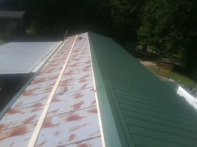 Old rusted panels beside newly installed green metal roofing — Wind Damage Roof Repair by Roofing Brothers in Gilman