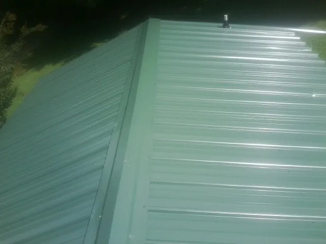 New green metal panels meeting at the ridge of a roof — Flat Roof Repair work by our crew in Gilman