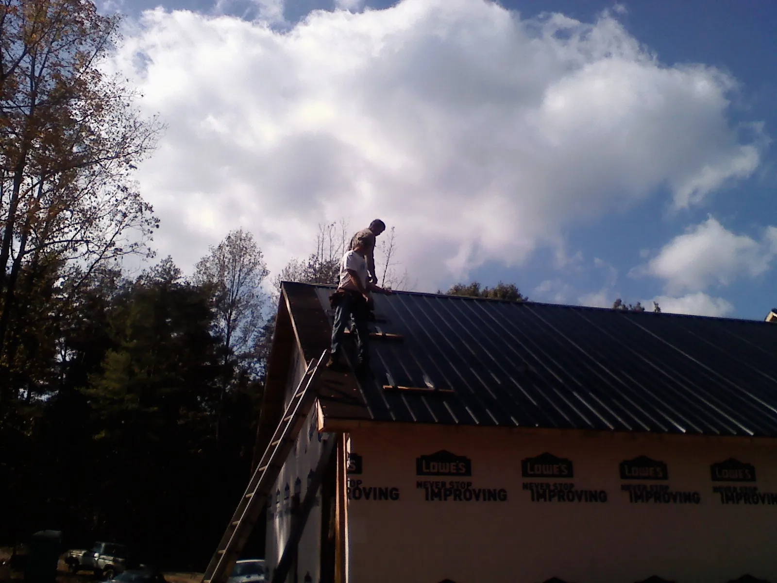 Roofer fastening dark metal panels high against a cloudy sky, from a Roof Inspection job in Gilman
