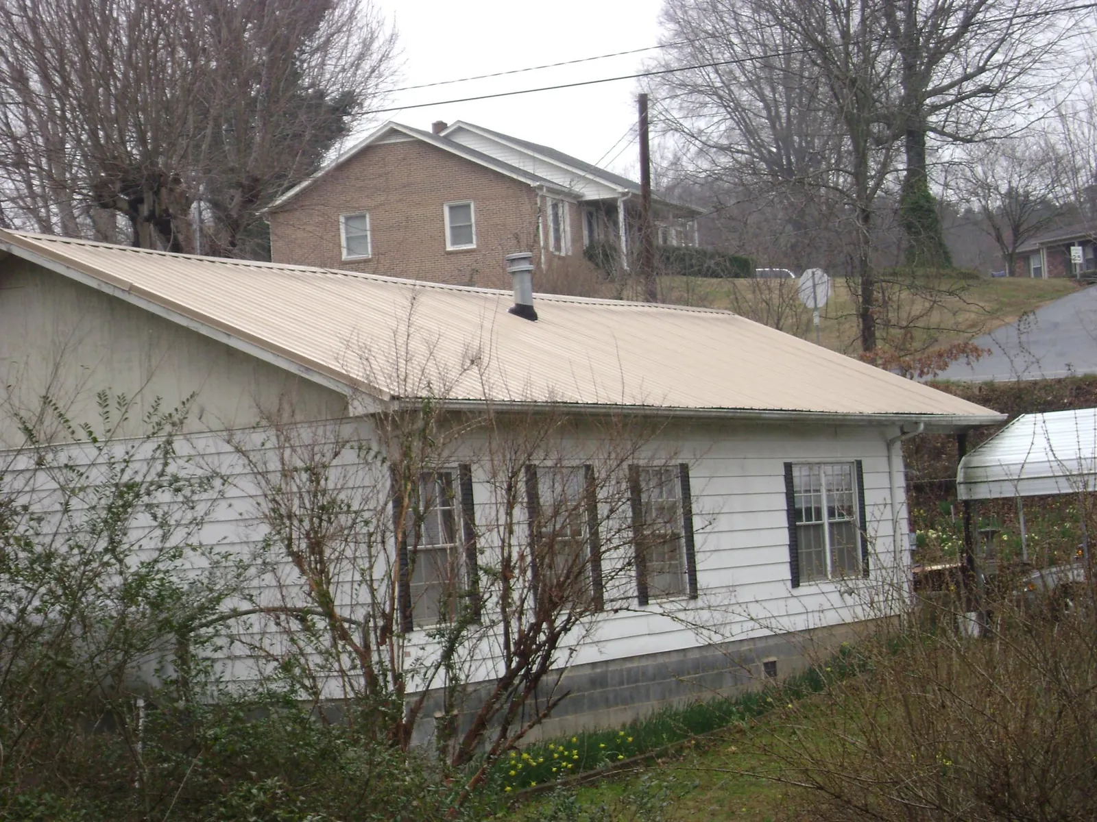 Tan metal roof on a white sided house set into a hillside — Commercial Roofing by Roofing Brothers in Gilman
